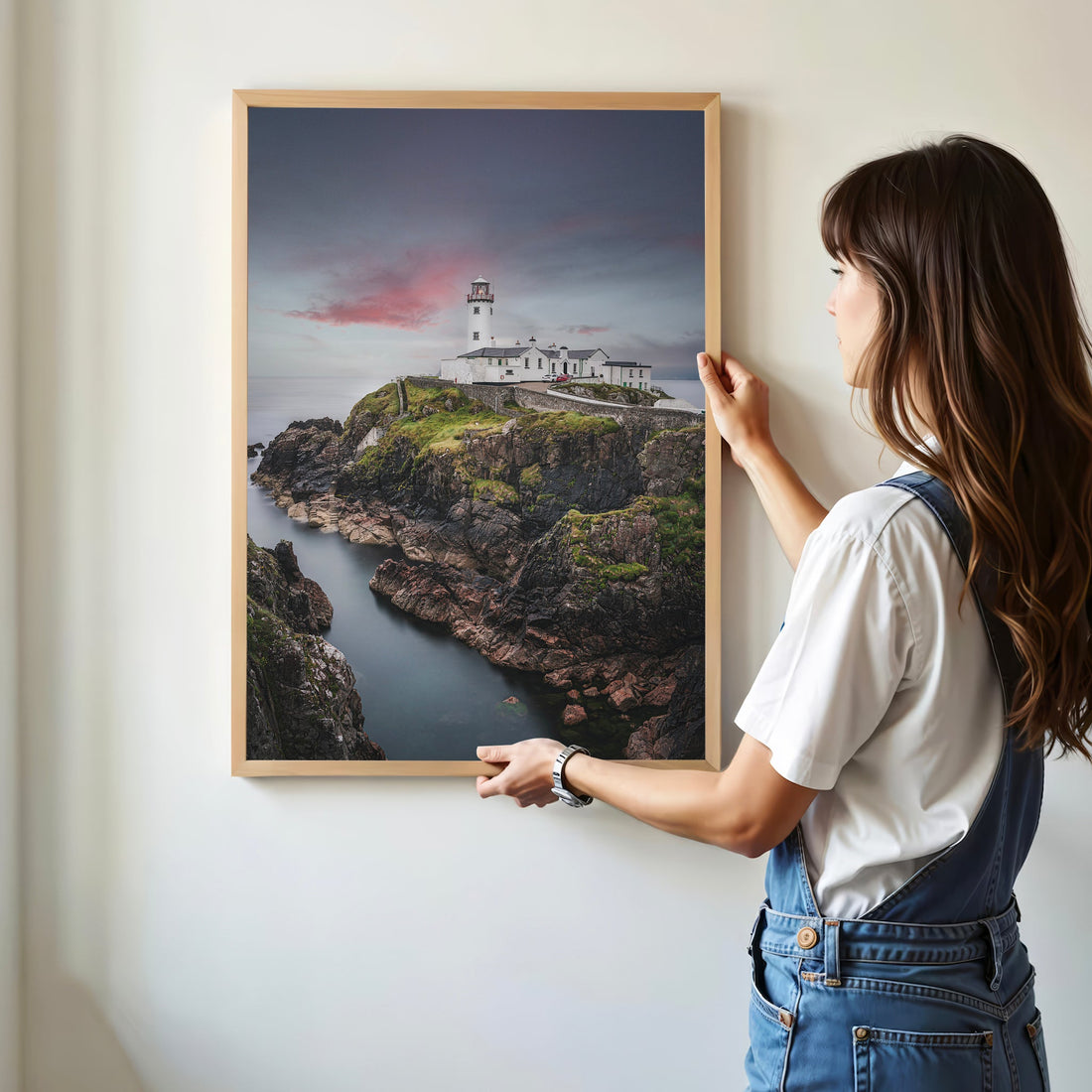 Woman hanging framed Fanad Lighthouse photo print on wall