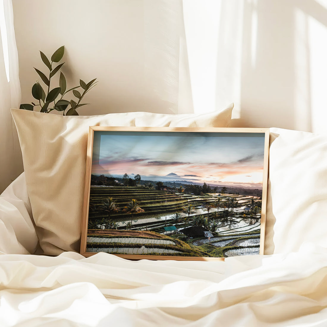 Natural wood framed Jatiluwih Rice Terraces sunrise print Bali Indonesia leaning against pillows in a bedroom setting