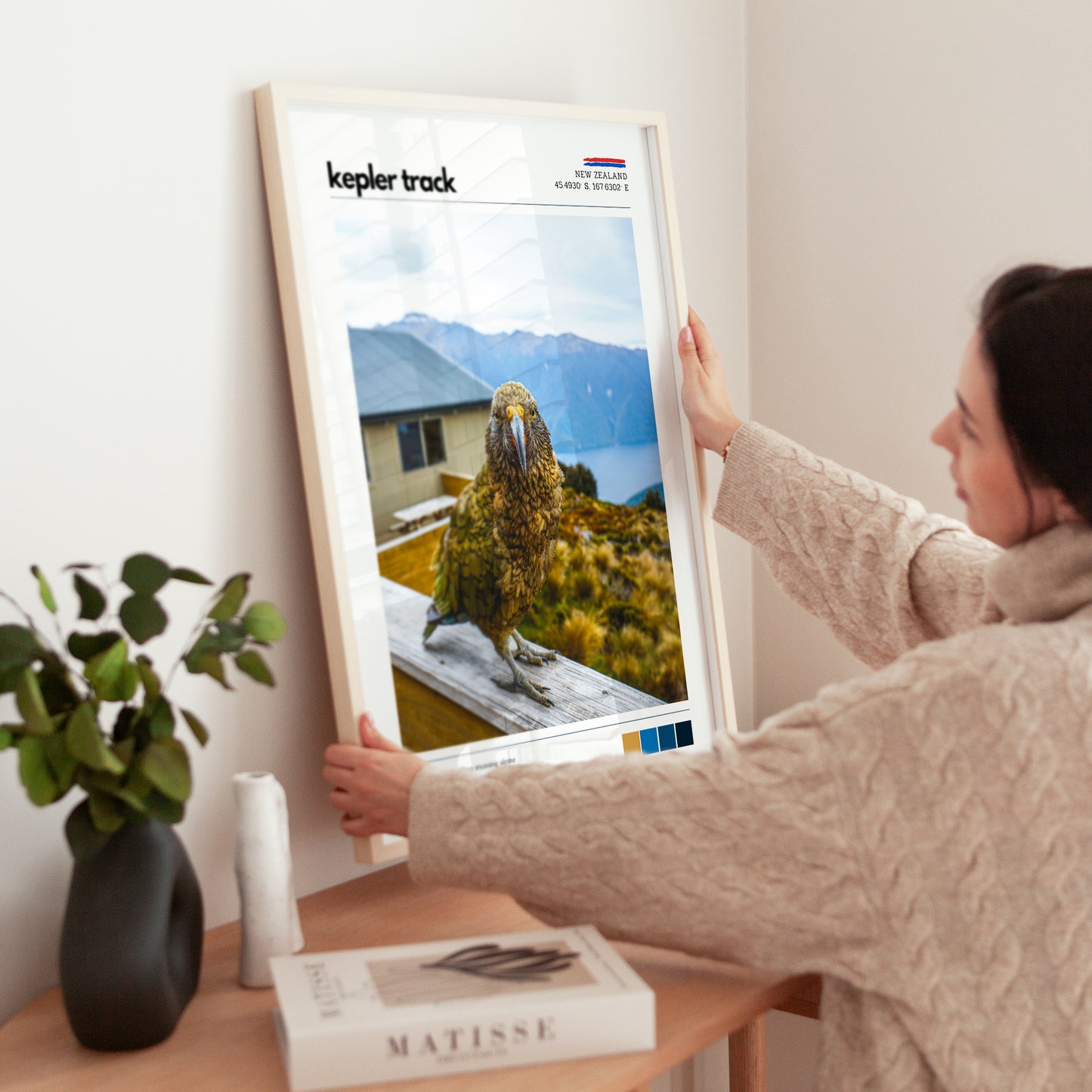 Hands placing a framed Kepler Track kea wall art print