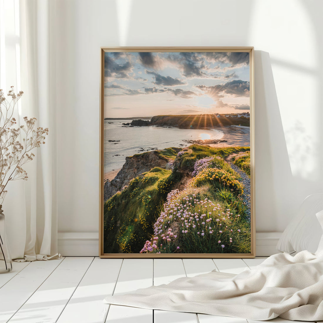 Framed Irish coastal wall art on white wooden floors, with sunlight hitting Annestown cliffs and flowers.