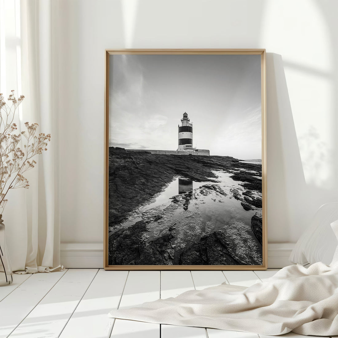 Framed lighthouse print on floor in white sunlit coastal-style room