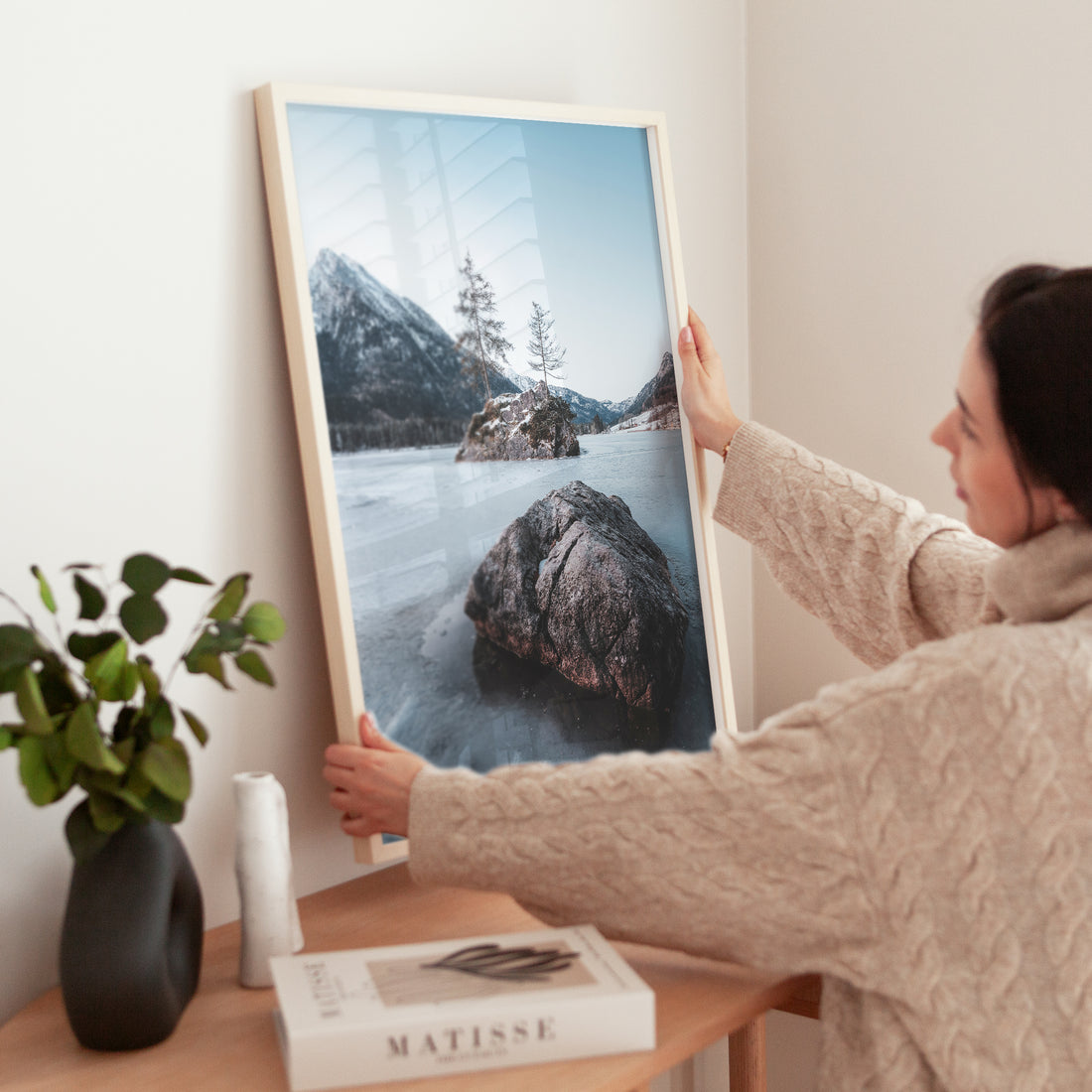 Woman adjusting a winter Hintersee lake print on wooden side table with Matisse book