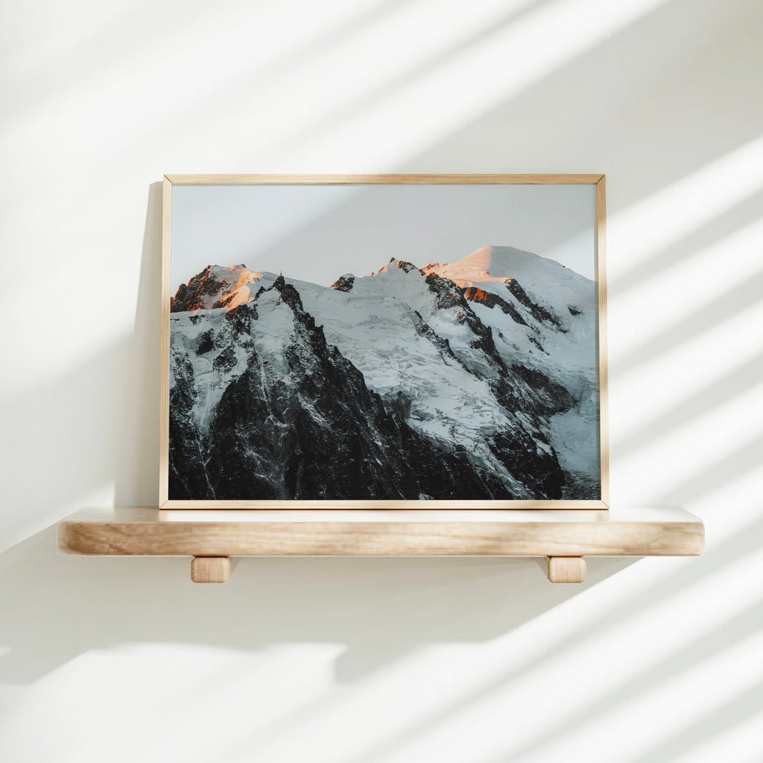 Wall print of Mont Blanc's snowy summit illuminated by warm alpine light above dark rugged spires.