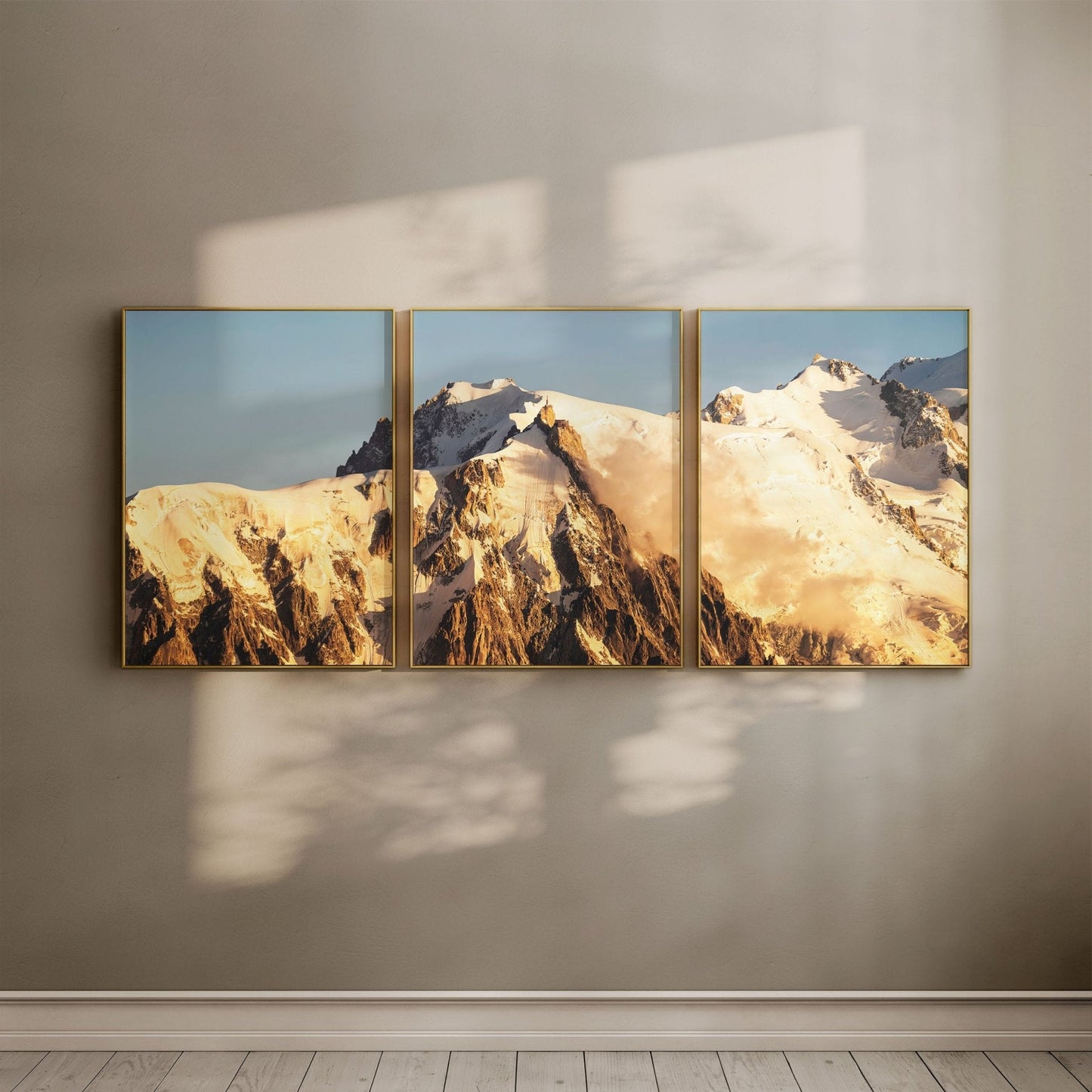Three-piece Mont Blanc sunrise wall art arranged in a gallery format, casting soft light and shadow across the room.
