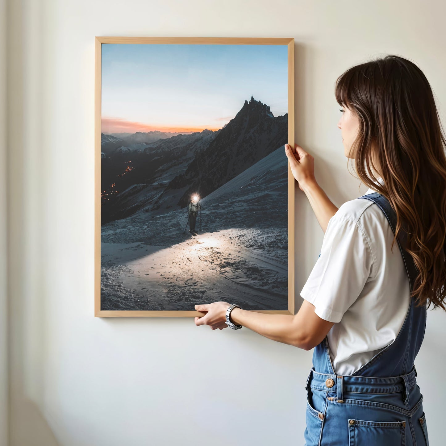 Woman hanging a framed alpine glacier print of a mountaineer at twilight