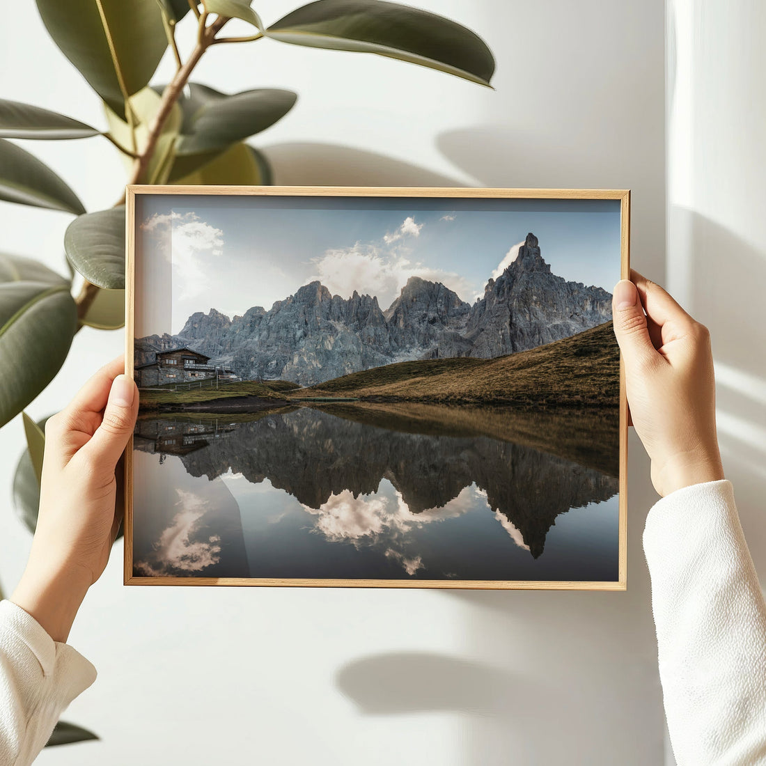Hands holding framed Passo Rolle reflection print with pale sky and mountain peaks