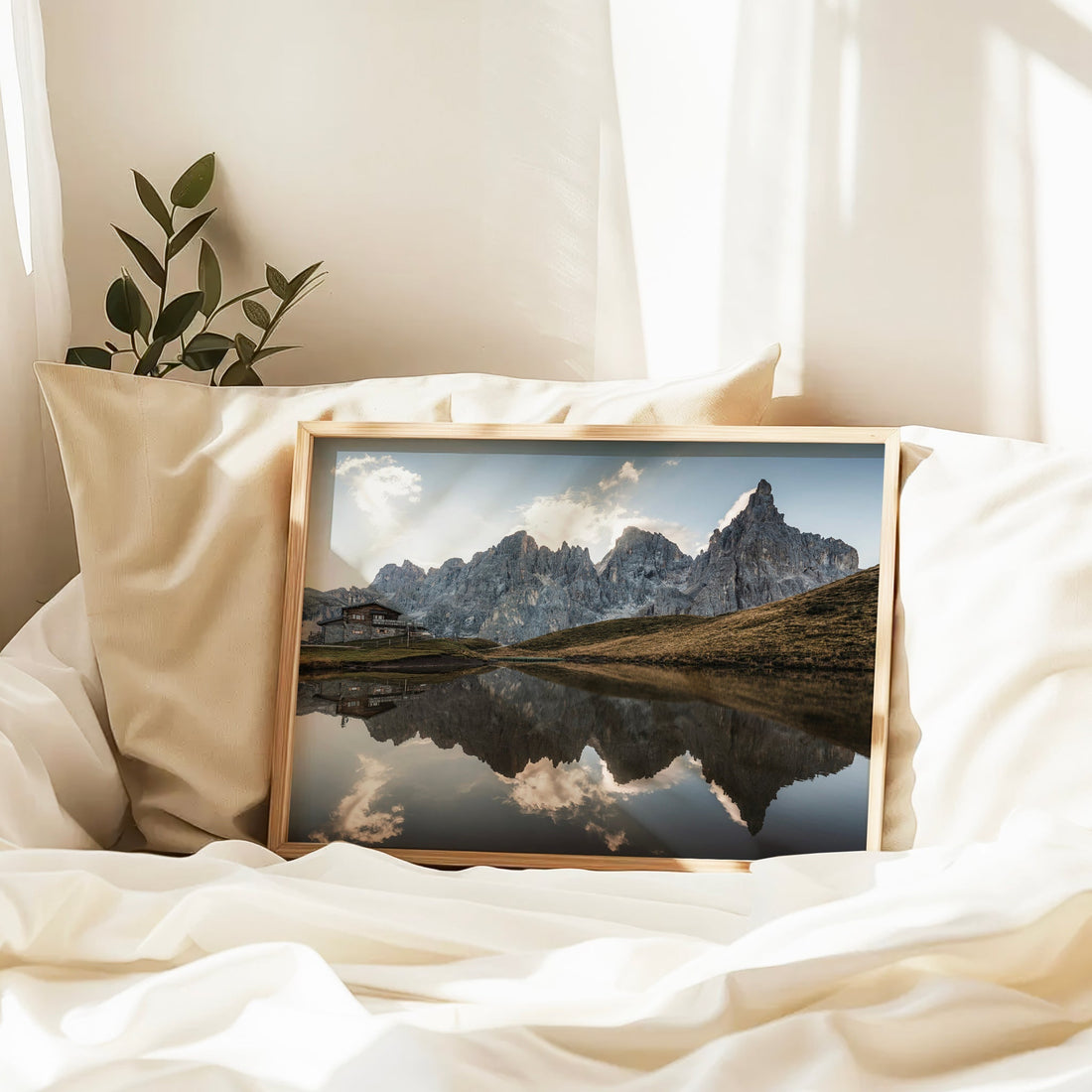 Framed Passo Rolle lake reflection print resting on soft bedding with gentle light