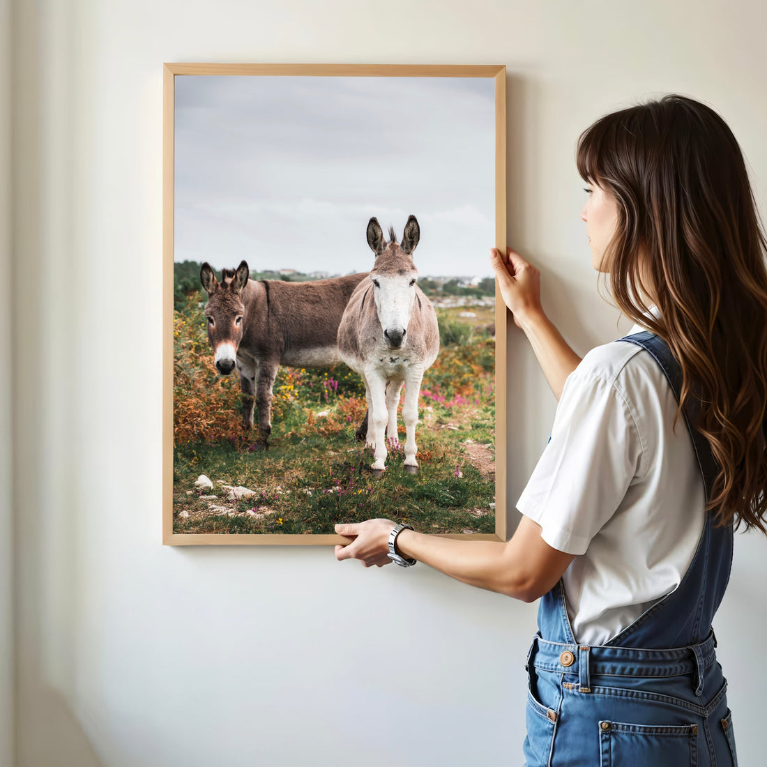 Framed donkey wall art being hung by a woman in a minimal home.