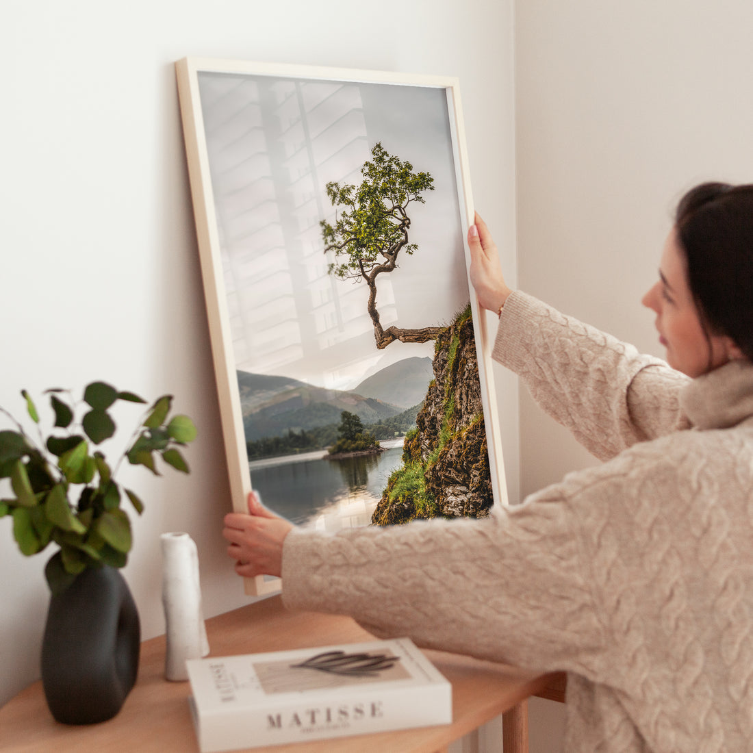 Woman placing a framed lake district tree print on a wooden table