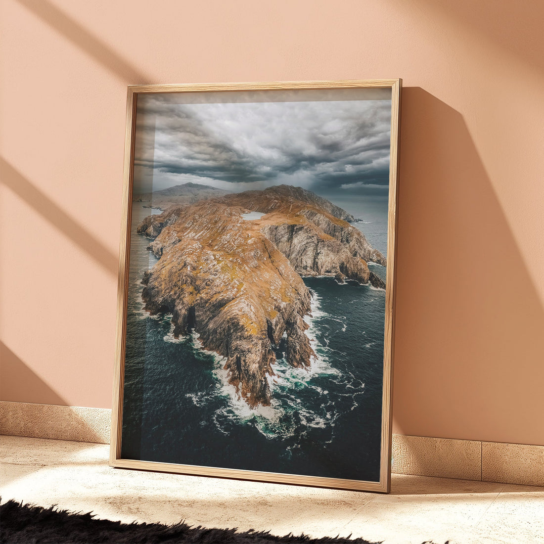 Framed print of Sheep’s Head Peninsula standing on wood floor in sunlit peach room.