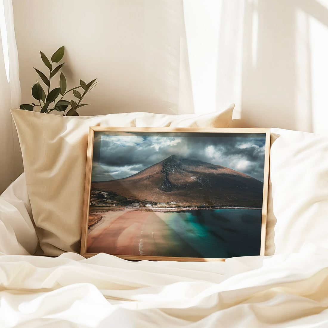 Dugort Beach print in wooden frame resting on white bedding with soft natural light.