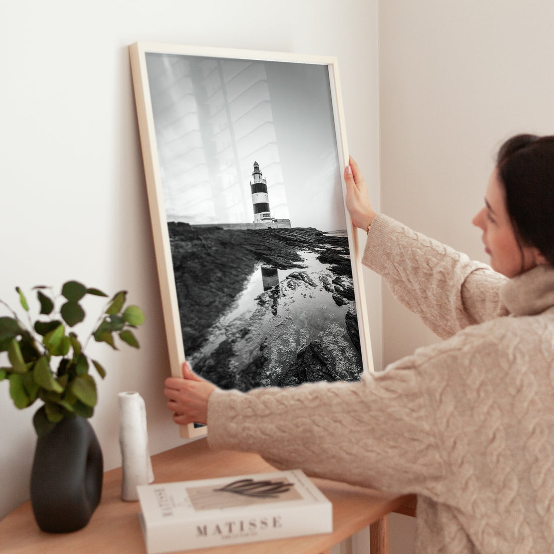 Woman adjusting Irish lighthouse wall art on sideboard with books