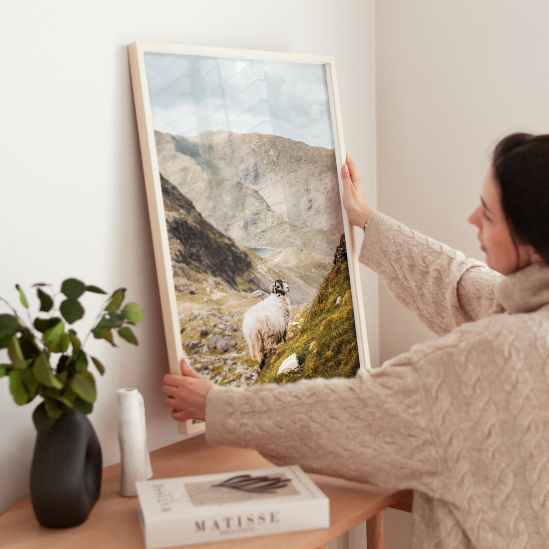 Woman placing a framed print of the Old Man of Coniston with a sheep in the frame.