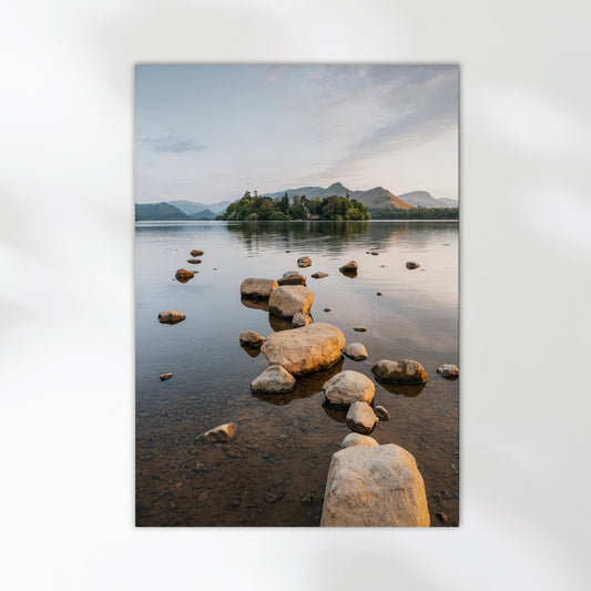 Stone path leading into Derwentwater during sunrise in the Lake District, with mountains in the distance