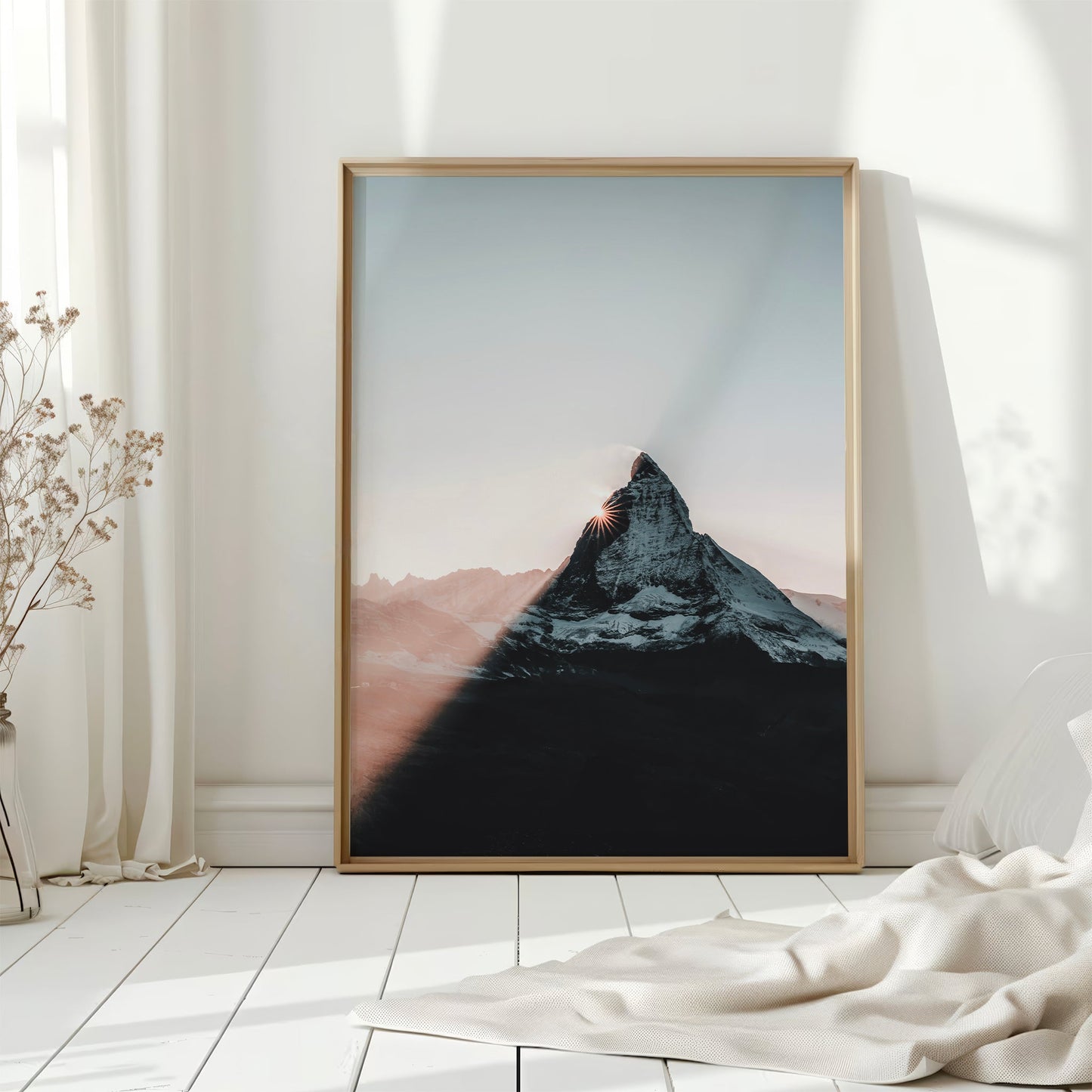 Framed Matterhorn print with sunset hues on floor by white curtains