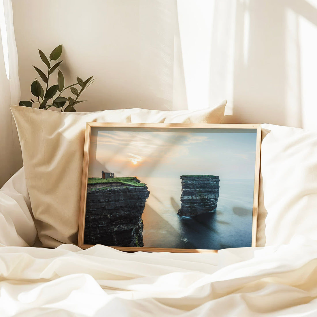 Downpatrick Head photo print resting on bed with soft pillows and early evening light