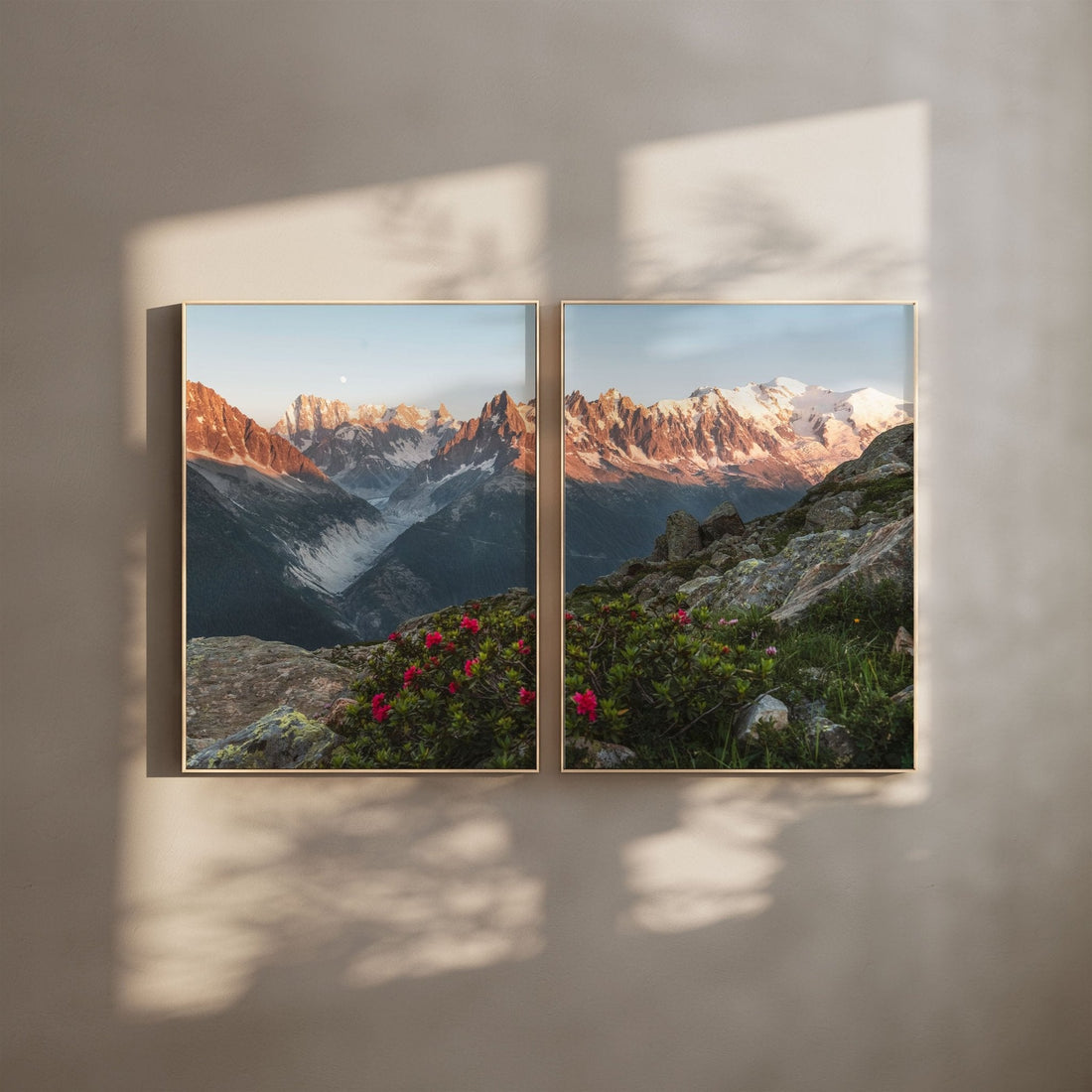 Framed wall art of a mountain landscape at sunset with pink wildflowers in the foreground, golden lighting, and dramatic peaks.