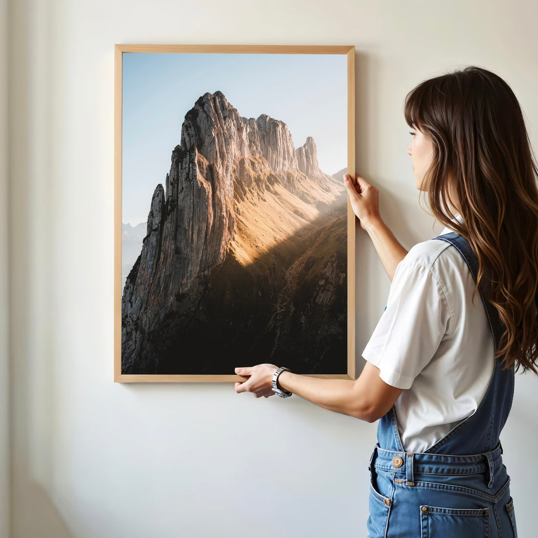 Woman hanging a Saxer Lücke Switzerland wall art print, vertical mountain scene.