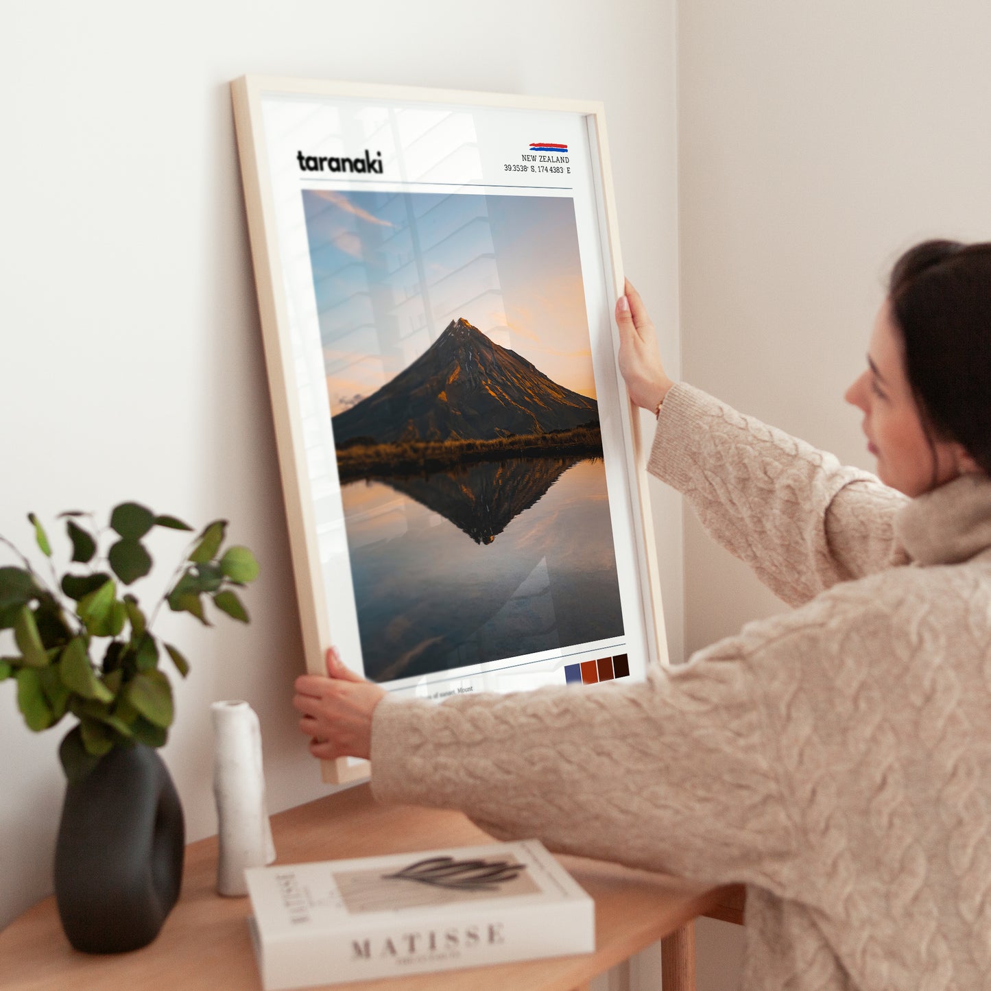 Hands adjusting a framed Mount Taranaki landscape wall art print in a calm living space