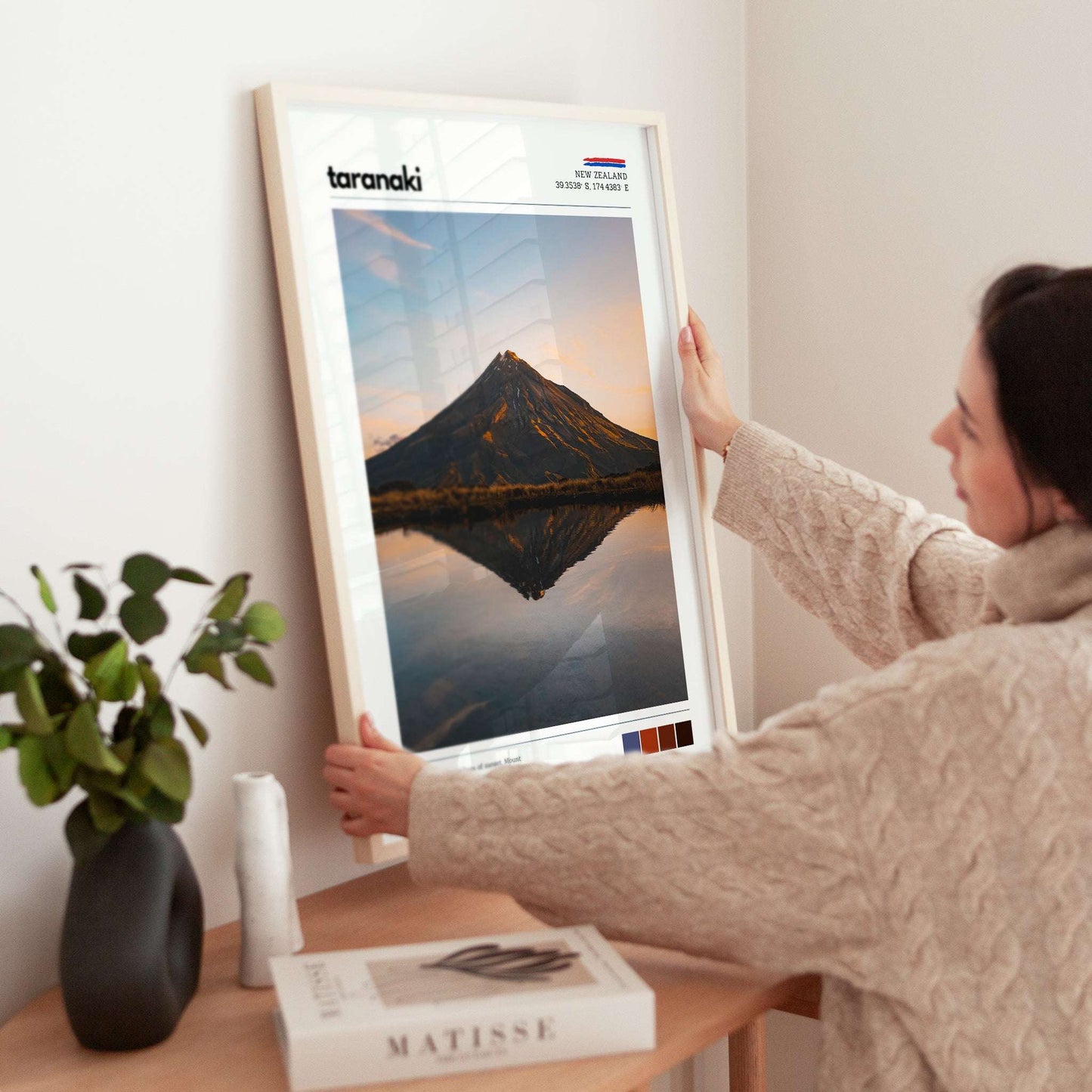Hands adjusting a framed Mount Taranaki landscape wall art print in a calm living space