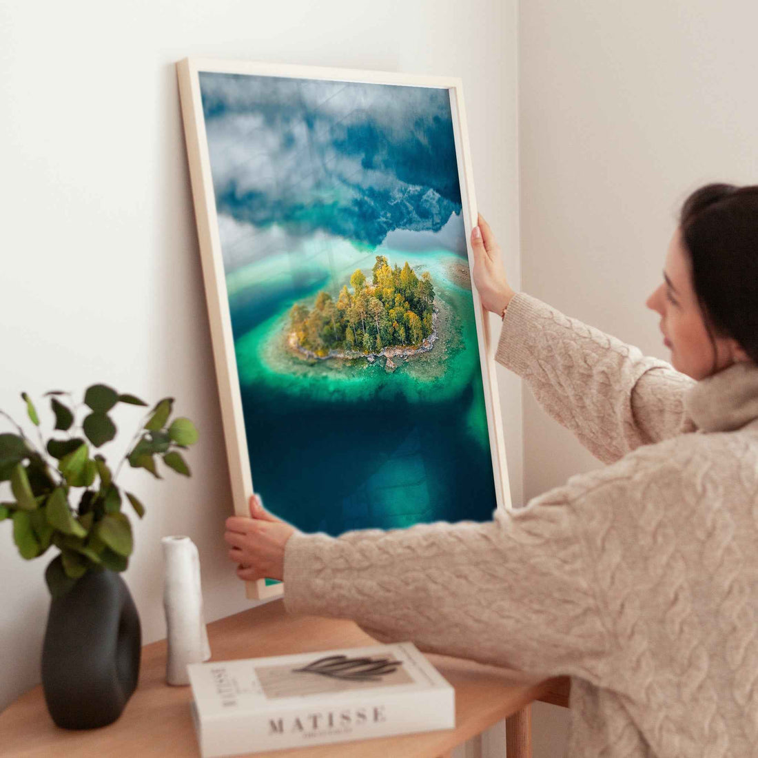 Woman placing aerial Eibsee island print on a wooden table in cosy interior