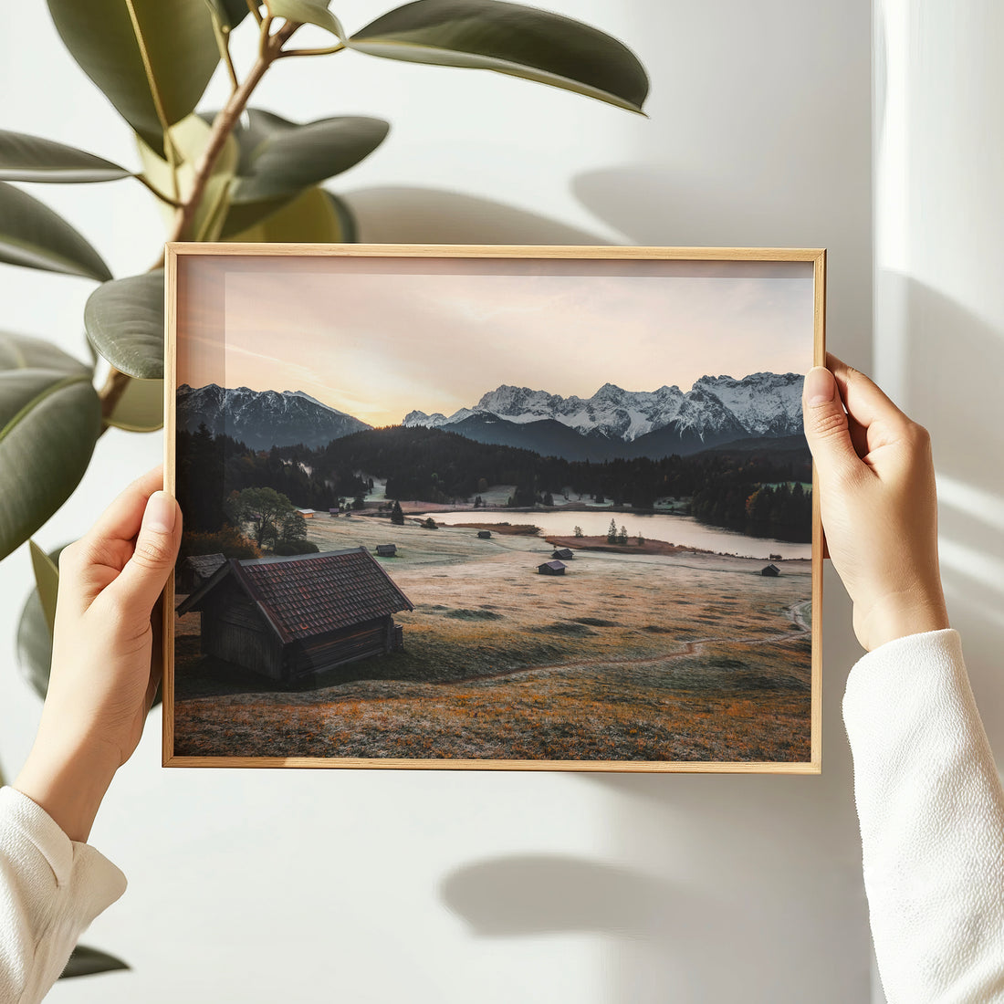 Woman hanging a Geroldsee landscape print with warm alpine tones