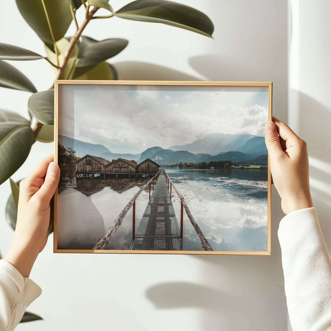 Woman hanging a Kochelsee boathouse landscape print on white wall