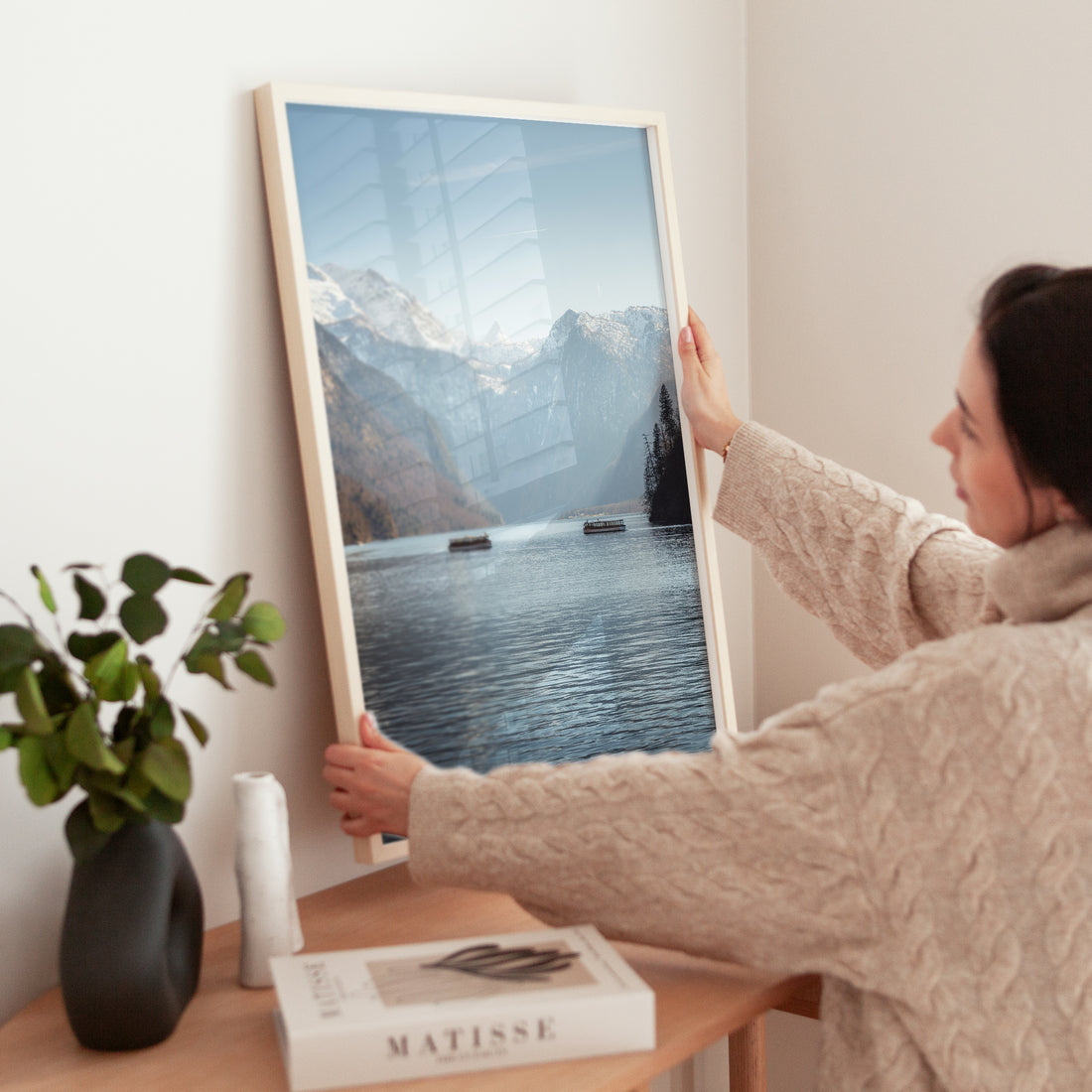 Woman placing a Königssee print on shelf beside a book and plant