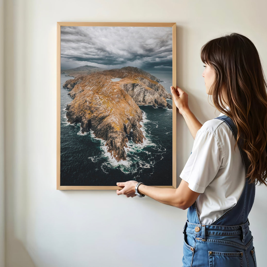 Woman hanging framed Sheep’s Head Peninsula print on a white wall.