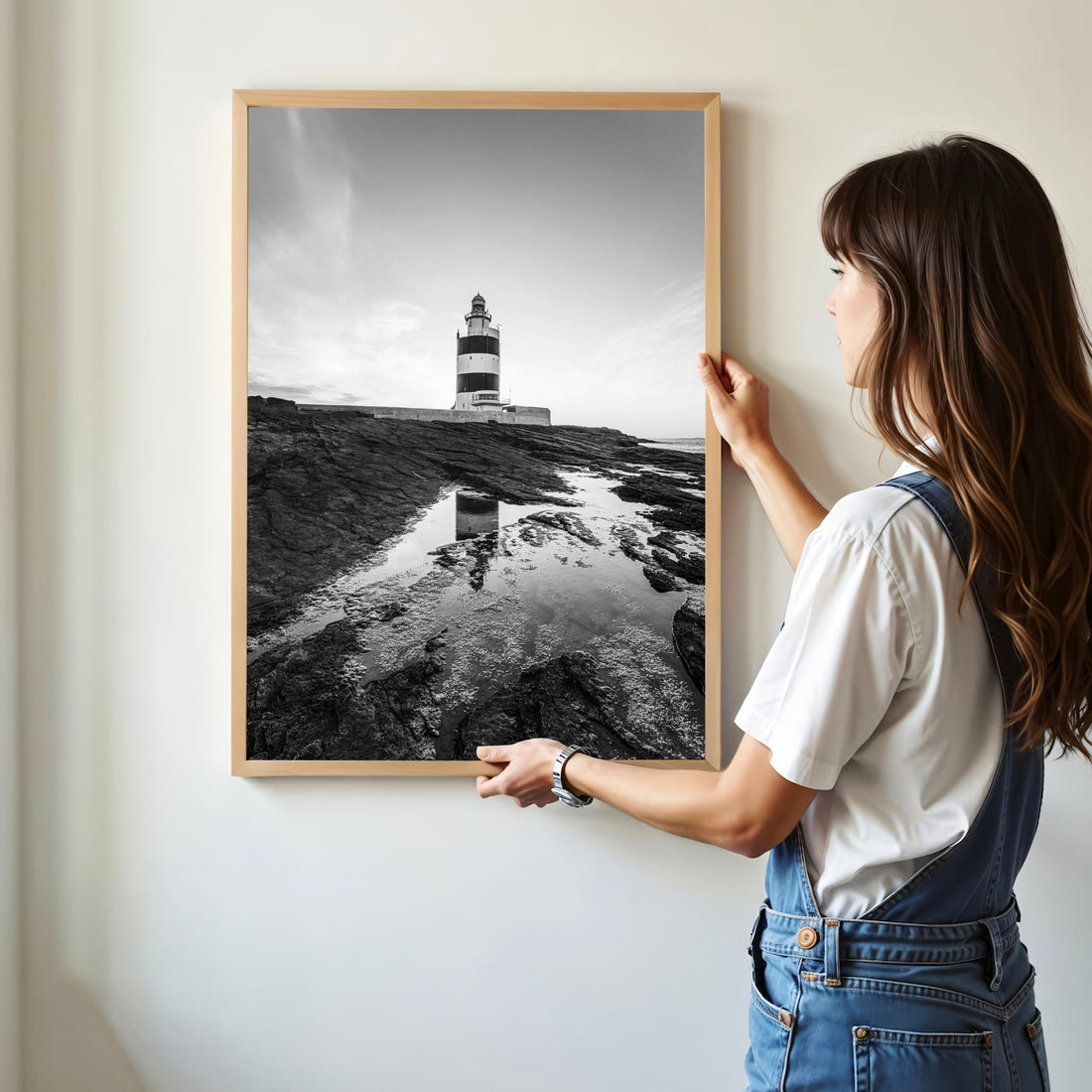 Woman hanging framed Hook Head Lighthouse print in minimalist room