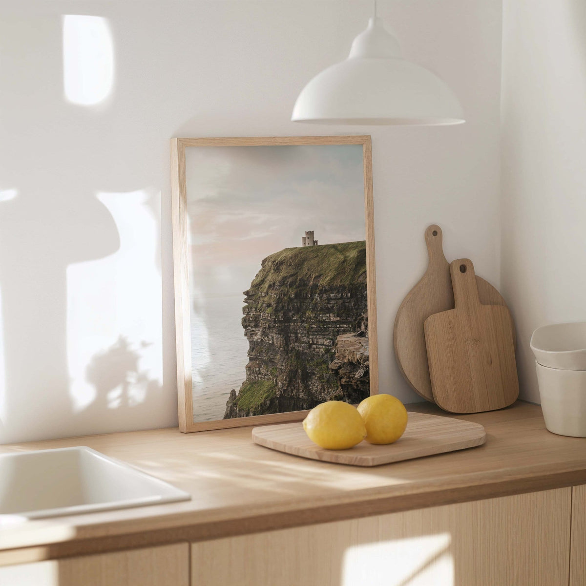 Cliffs of Moher coastal print in white frame on a kitchen counter with wooden boards, yellow lemons and white pendant lamp