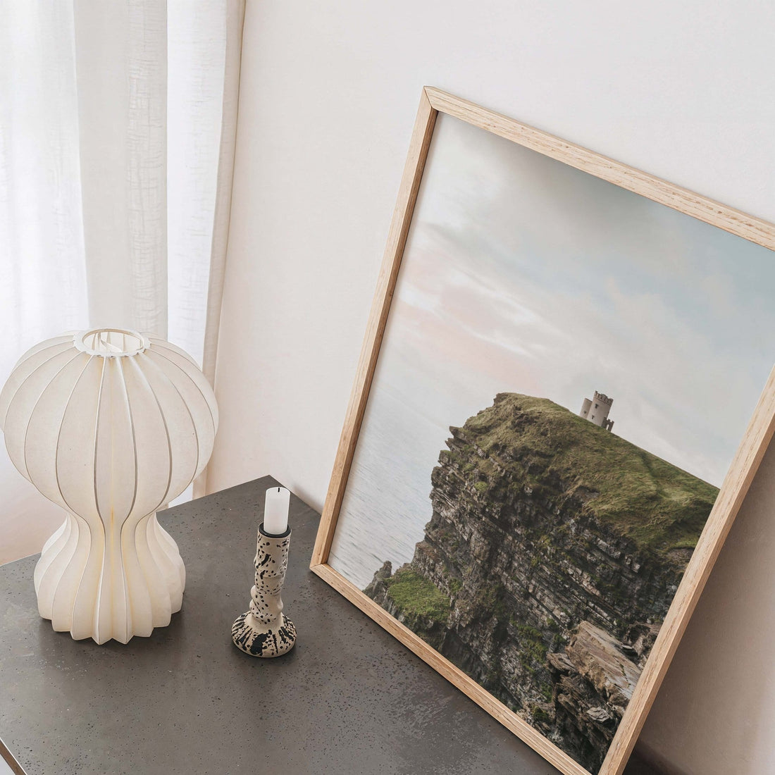 Cliffs of Moher print in white frame styled on a dark tabletop surface with a white lamp and small candlestick