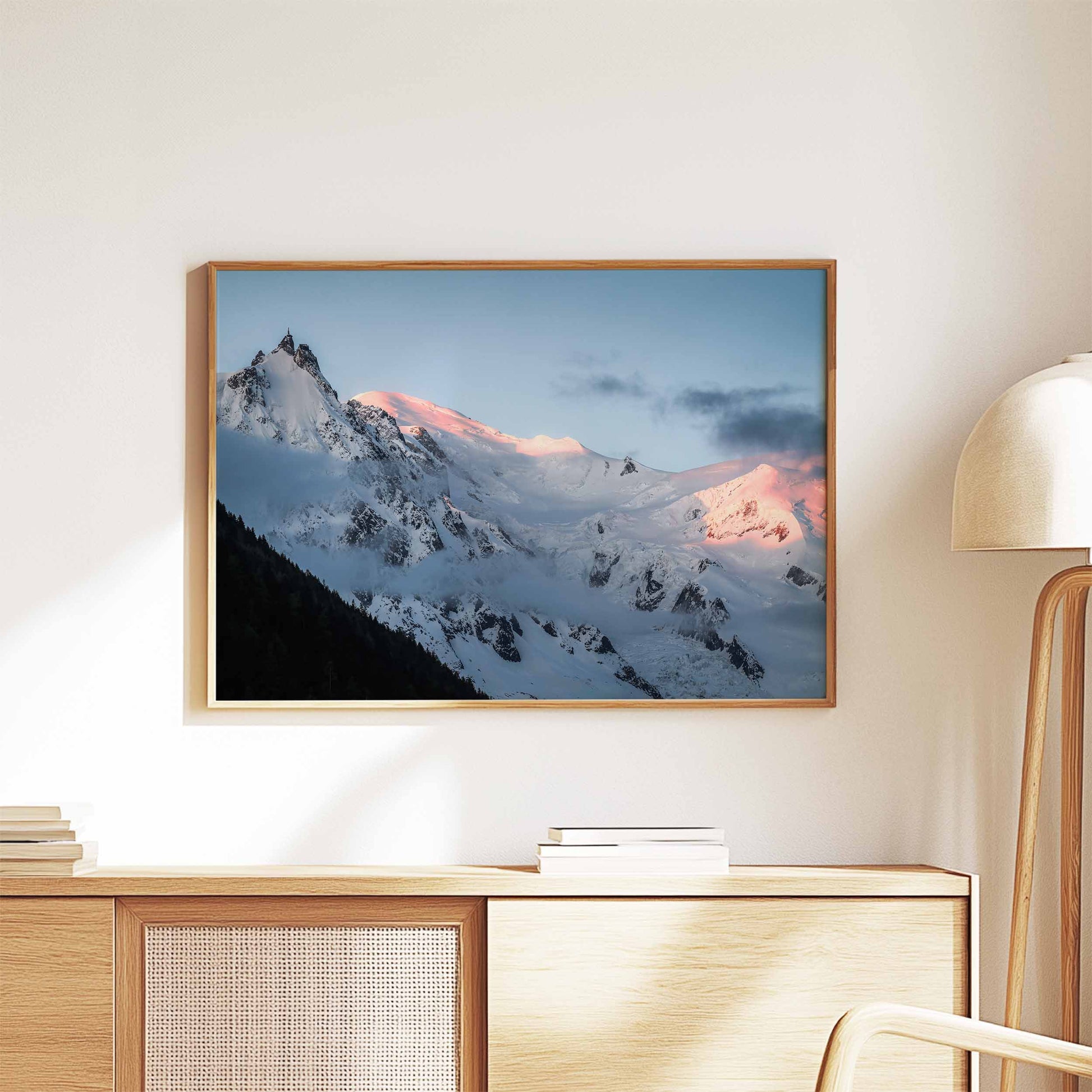 Beautiful alpenglow print of the Aiguille du Midi, framed and styled on a wooden cabinet for a warm decor touch.