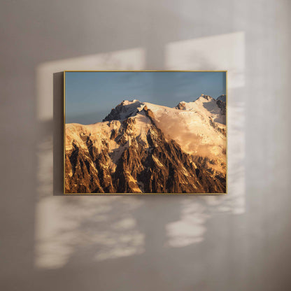 Framed wall art print of the Aiguille du Midi glowing warmly in golden sunset light, styled with soft shadows.