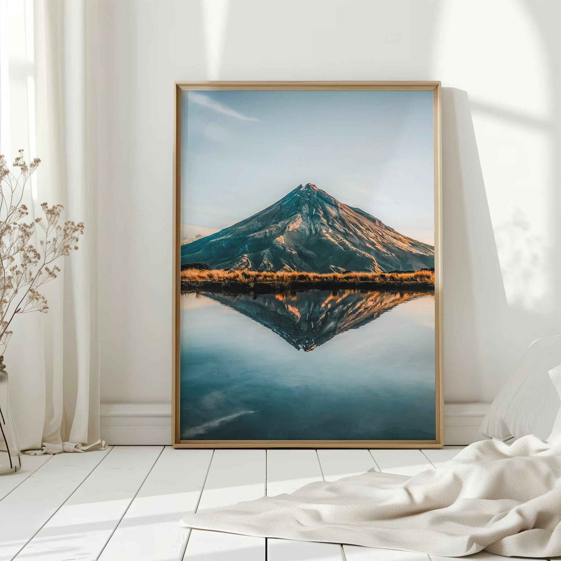 Natural wood framed Mount Taranaki reflection print leaning against white wall on white floorboards in minimal Scandinavian interior
