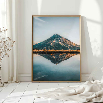 Natural wood framed Mount Taranaki reflection print leaning against white wall on white floorboards in minimal Scandinavian interior