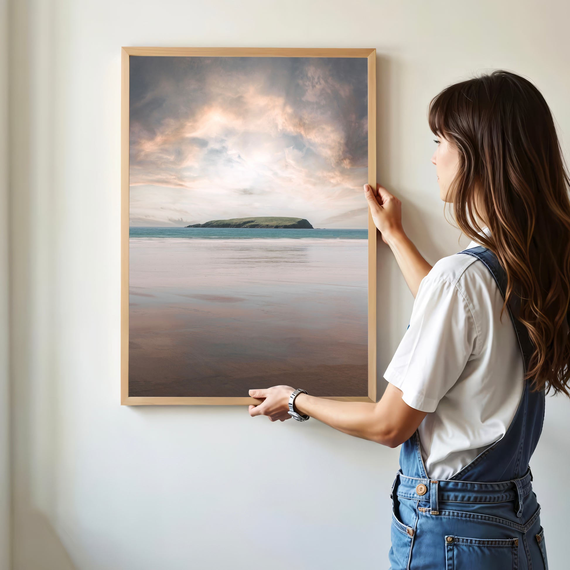 Woman hanging framed Keel Beach print featuring soft pastel tones and Irish coast