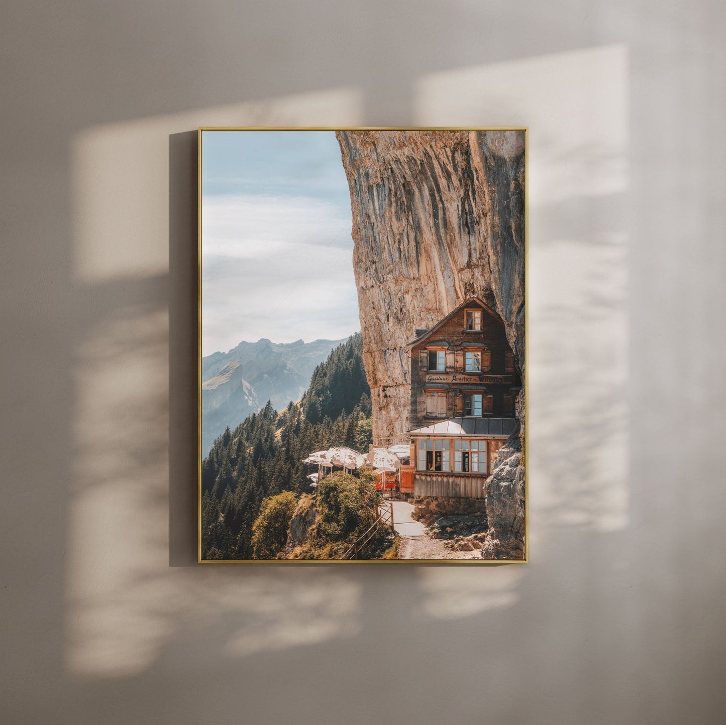 The Aescher Guesthouse nestled against a cliff in the Swiss Alps, framed in gold for a rustic yet elegant look.