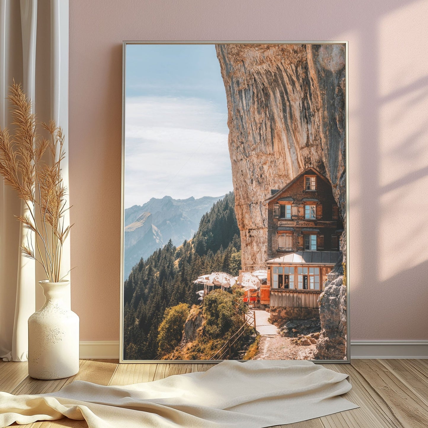 A stunning silver-framed photo of the Aescher Guesthouse perched against a sheer rock face, with alpine peaks in the distance.