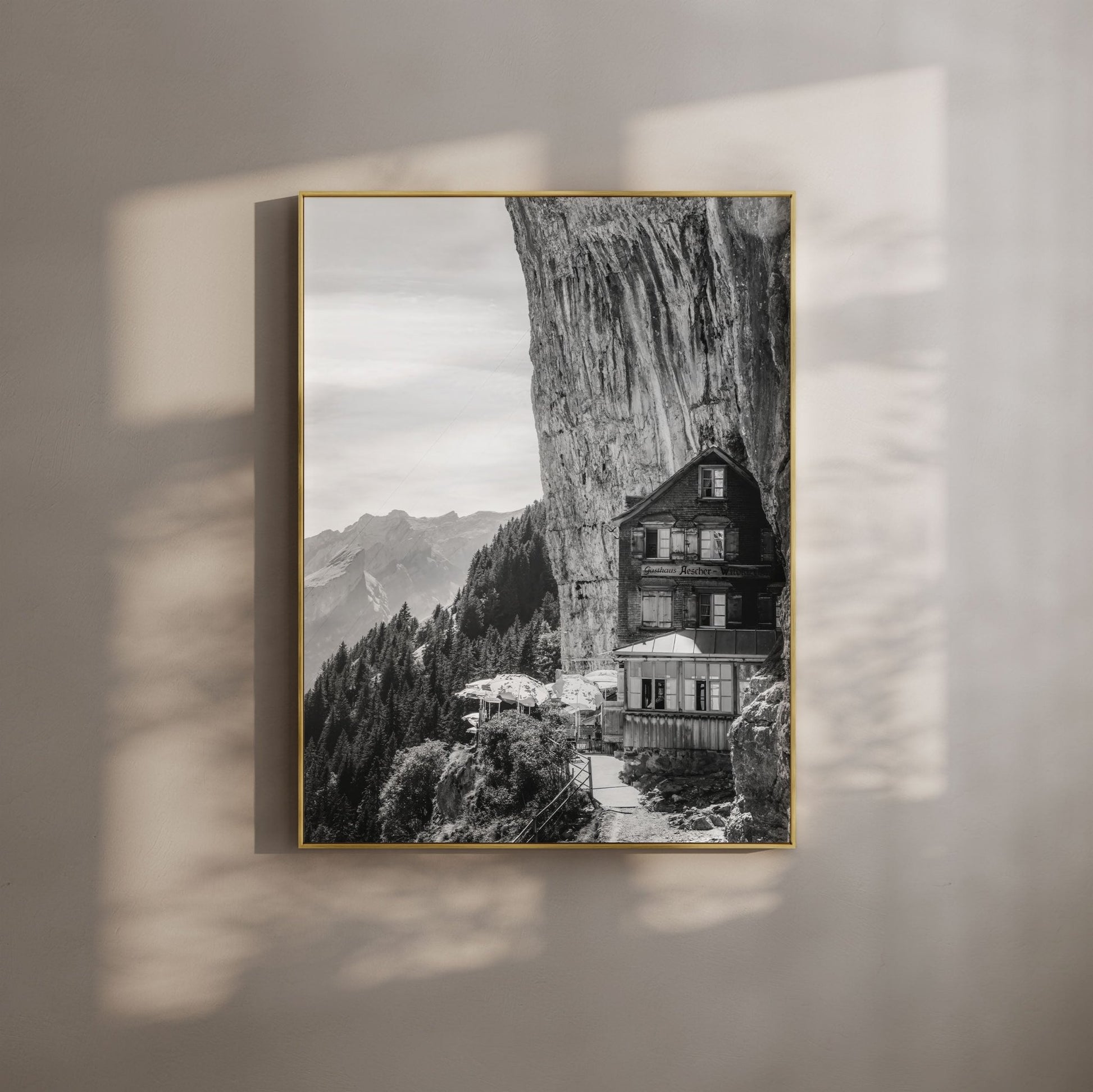 Black-and-white image of Aescher Guesthouse in Switzerland, nestled against a dramatic cliff with alpine peaks in the background, perfect for wall art.