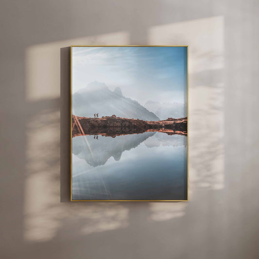  A serene alpine lake reflecting a mountain range, with two hikers walking along the ridge at sunrise.