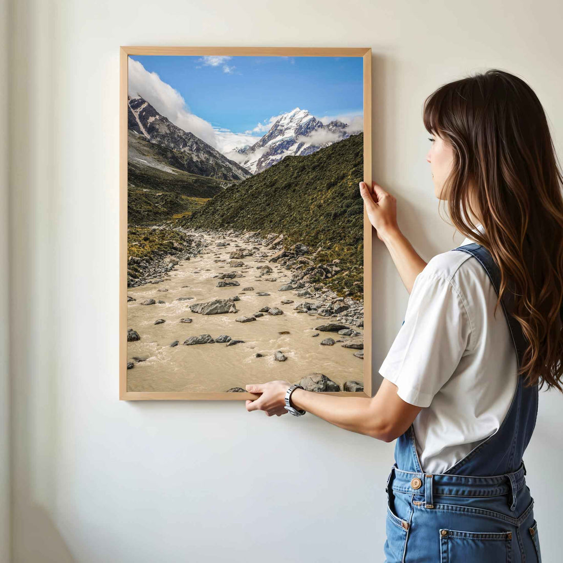 Woman hanging a natural wood framed Aoraki Mount Cook Hooker Valley New Zealand print on a white wall