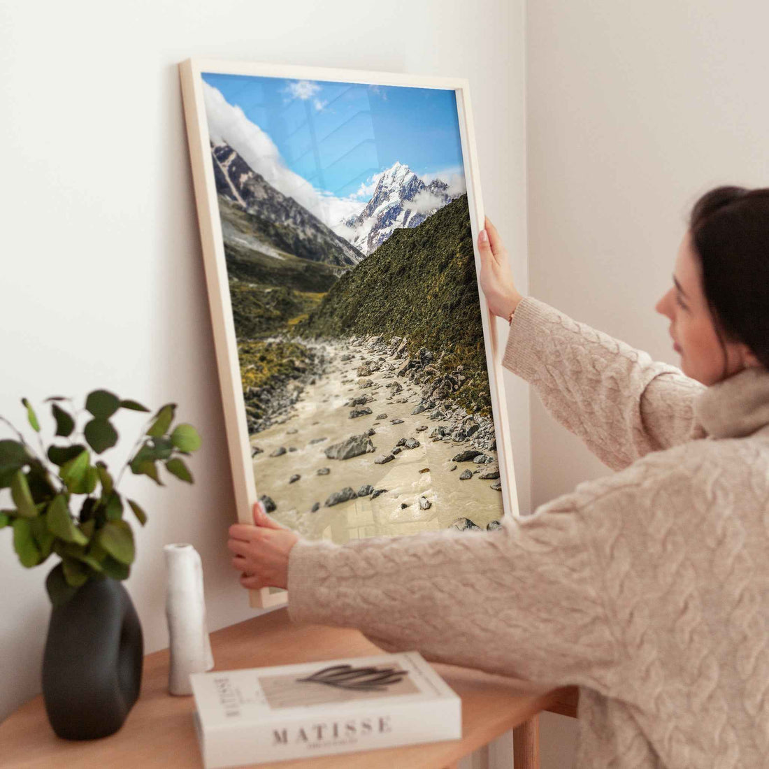 Woman placing a natural wood framed Aoraki Mount Cook Hooker Valley New Zealand print on a wooden sideboard