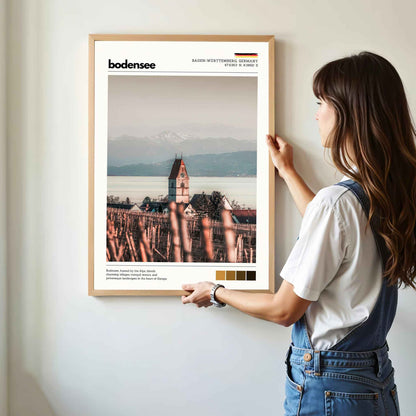 Woman hanging framed Bodensee Lake Constance Germany church and vineyard photography print in natural oak frame on white wall