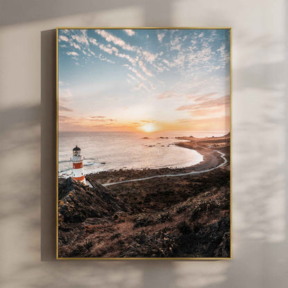 Framed Cape Palliser lighthouse sunset photography print in gold float frame mounted on warm beige wall with window light shadows