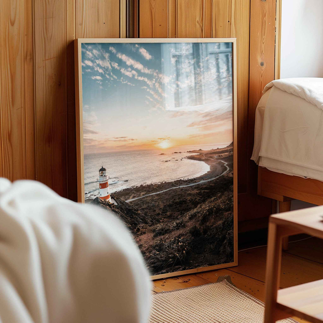 Framed Cape Palliser lighthouse sunset print in natural wood frame leaning against pine panelled bedroom wall