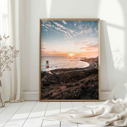 Natural wood framed Cape Palliser lighthouse sunset print leaning against white wall on white floorboards in minimal Scandinavian interior