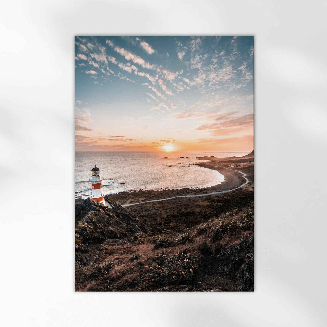 Unframed Cape Palliser lighthouse fine art print on white background showing red and white striped lighthouse at sunset over curved coastline