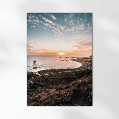 Unframed Cape Palliser lighthouse fine art print on white background showing red and white striped lighthouse at sunset over curved coastline