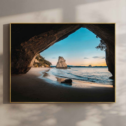 Framed Cathedral Cove sunrise landscape photography print in gold float frame mounted on warm beige wall with window light shadows